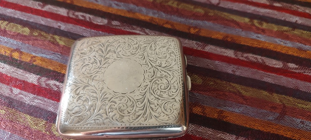 A square Victorian sterling silver cigarette case featuring hand-engraved foliate scrollwork and a blank central scalloped cartouche. View XVII