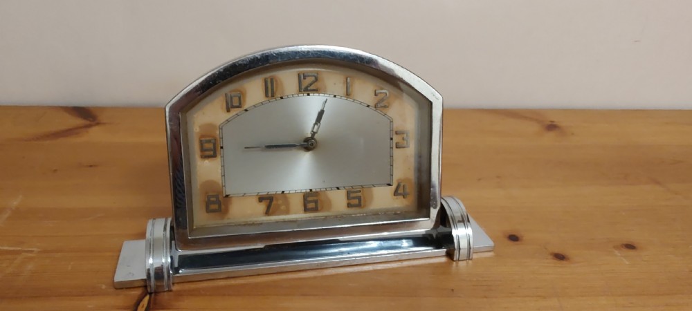 An Art Deco chrome mantel clock featuring an arched frame, stepped base, and a central dial with stylised geometric numerals.