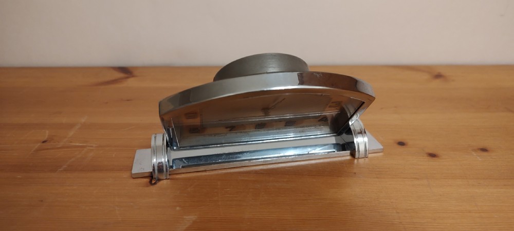 An Art Deco chrome mantel clock featuring an arched frame, stepped base, and a central dial with stylised geometric numerals. View III
