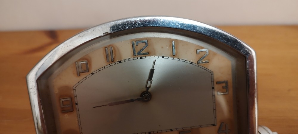 An Art Deco chrome mantel clock featuring an arched frame, stepped base, and a central dial with stylised geometric numerals. View IV