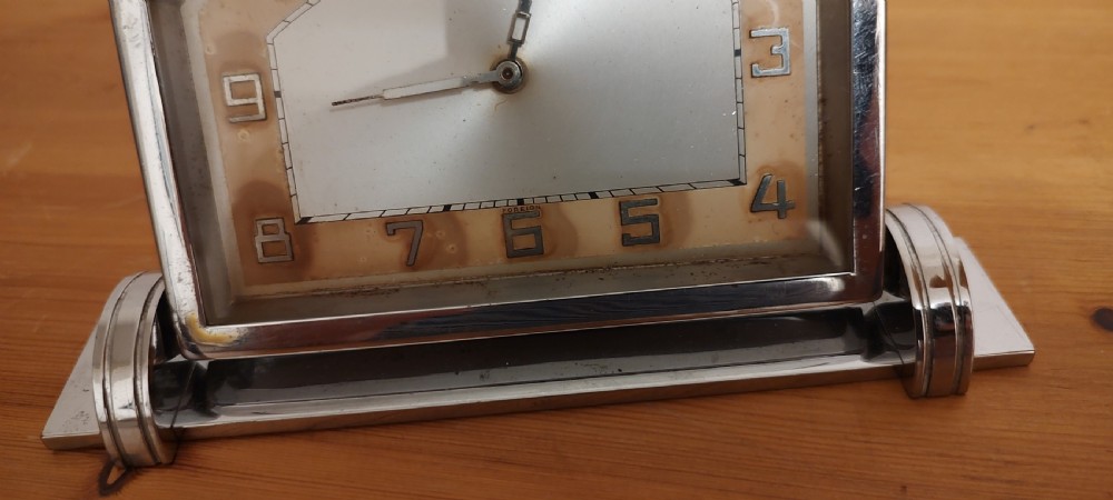 An Art Deco chrome mantel clock featuring an arched frame, stepped base, and a central dial with stylised geometric numerals. View V