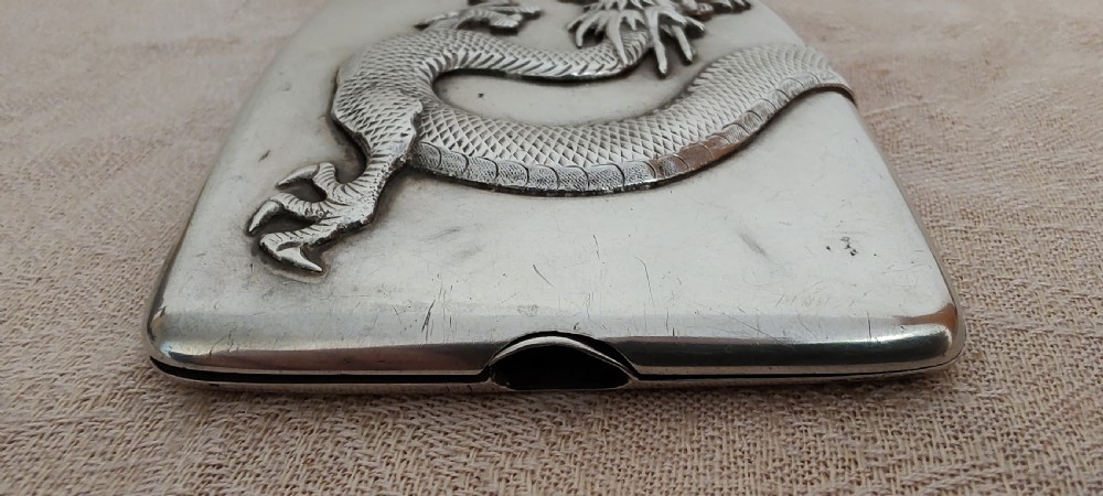 A rectangular silver Art Deco cigarette case featuring a detailed raised dragon motif across the front surface. View II