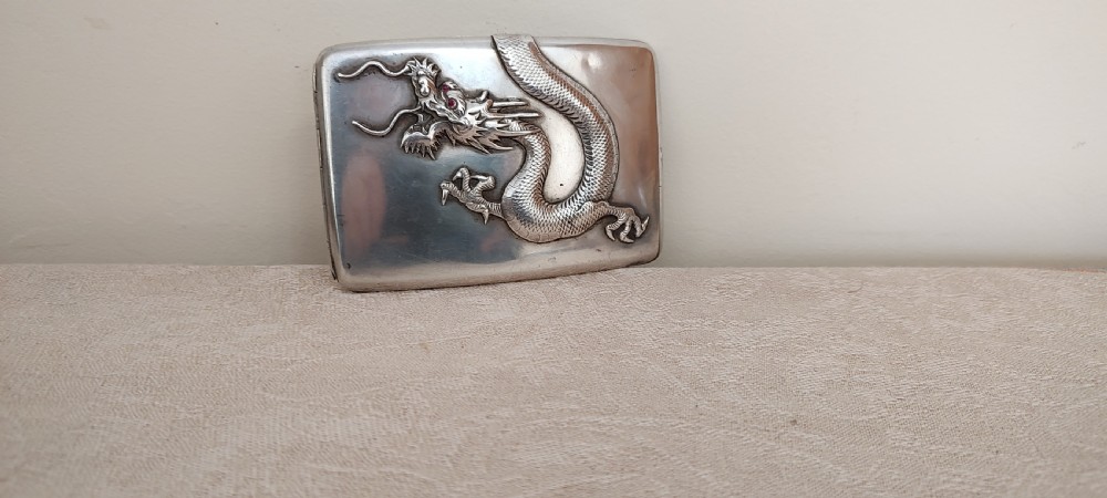 A rectangular silver Art Deco cigarette case featuring a detailed raised dragon motif across the front surface.