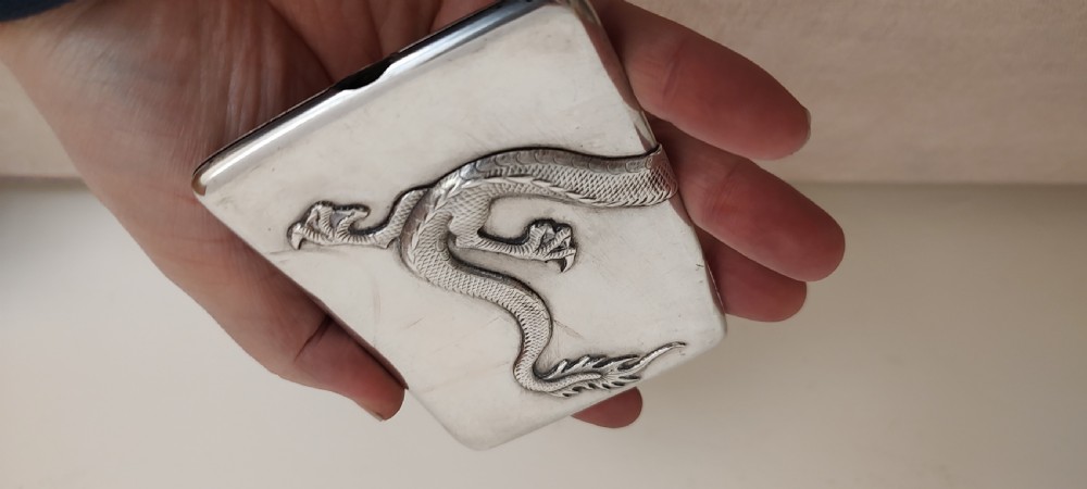 A rectangular silver Art Deco cigarette case featuring a detailed raised dragon motif across the front surface. View VI