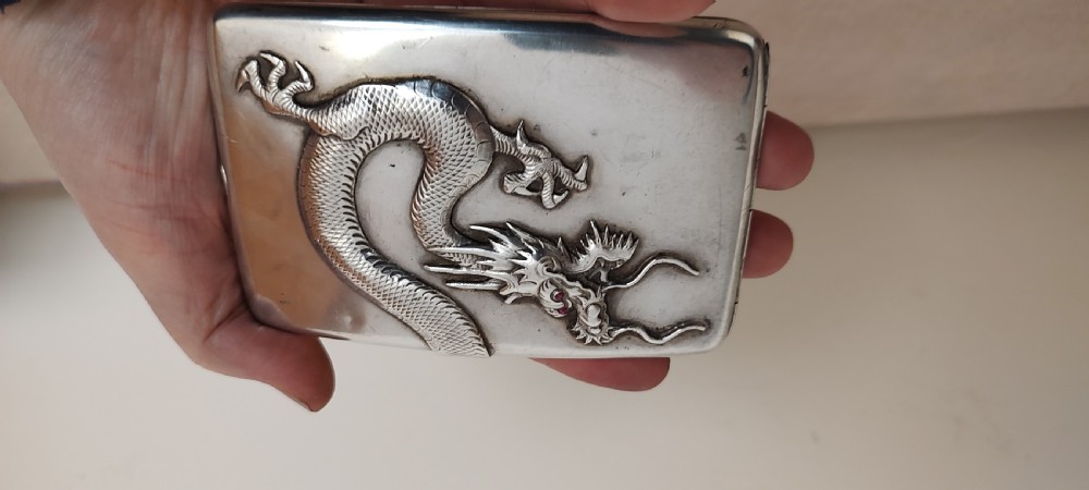 A rectangular silver Art Deco cigarette case featuring a detailed raised dragon motif across the front surface. View XII