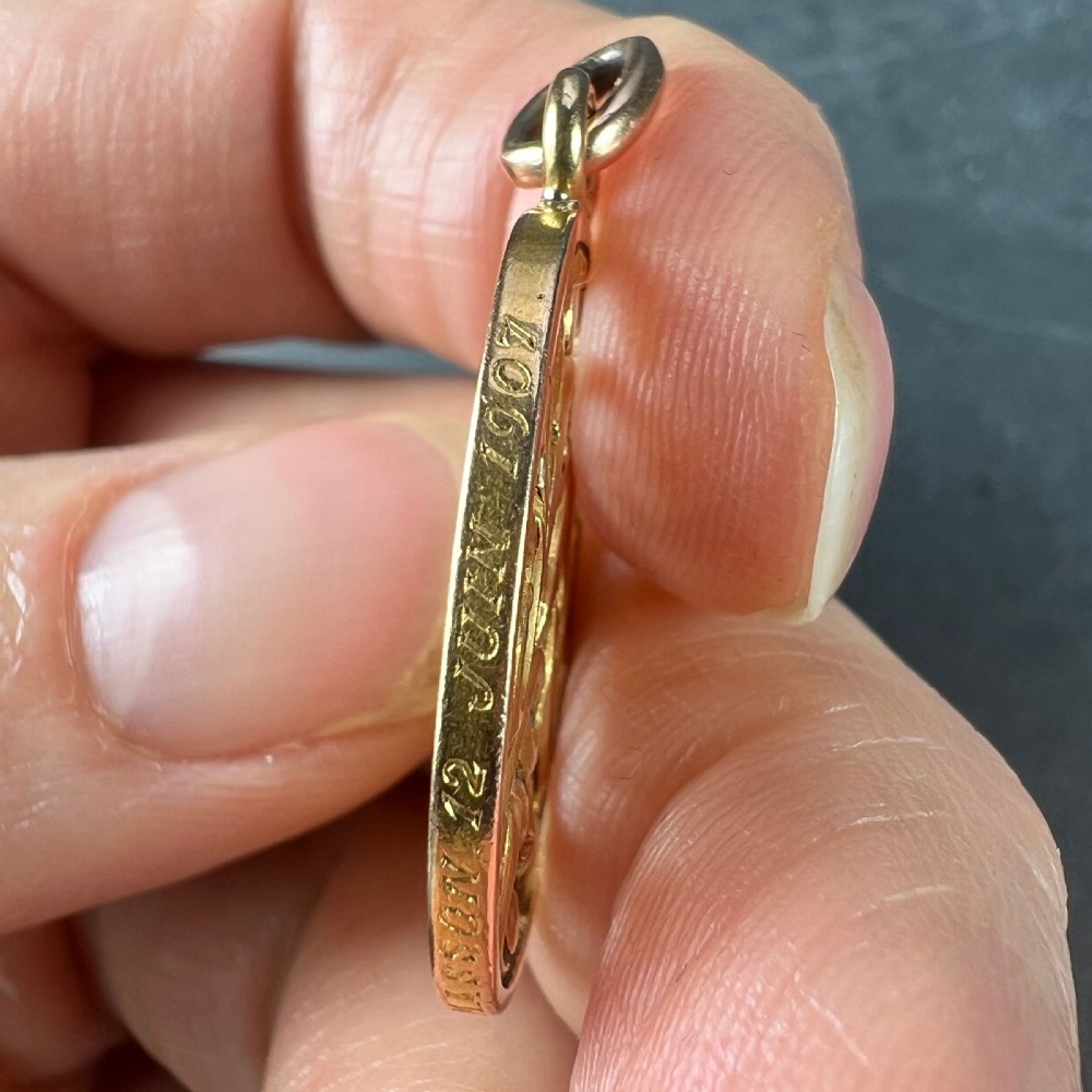 An oval 18ct yellow gold pendant featuring an intricate openwork monogram within a gold frame and suspension loop. View IV