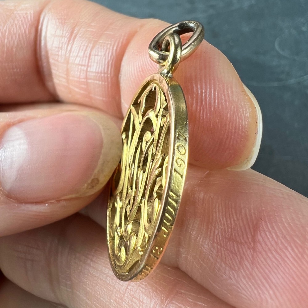 An oval 18ct yellow gold pendant featuring an intricate openwork monogram within a gold frame and suspension loop. View X