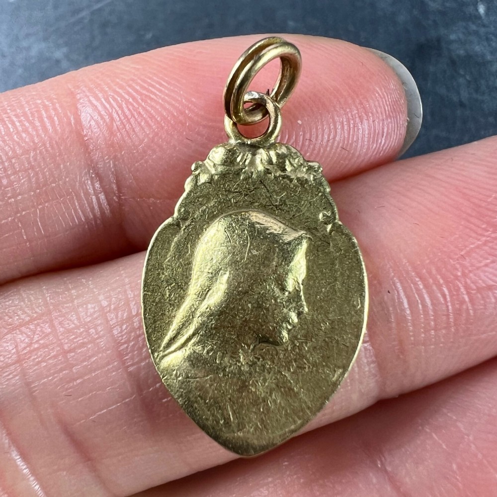 An oval 18K yellow gold religious pendant featuring a relief profile of the Virgin Mary against a textured background with a top suspension loop. View VI
