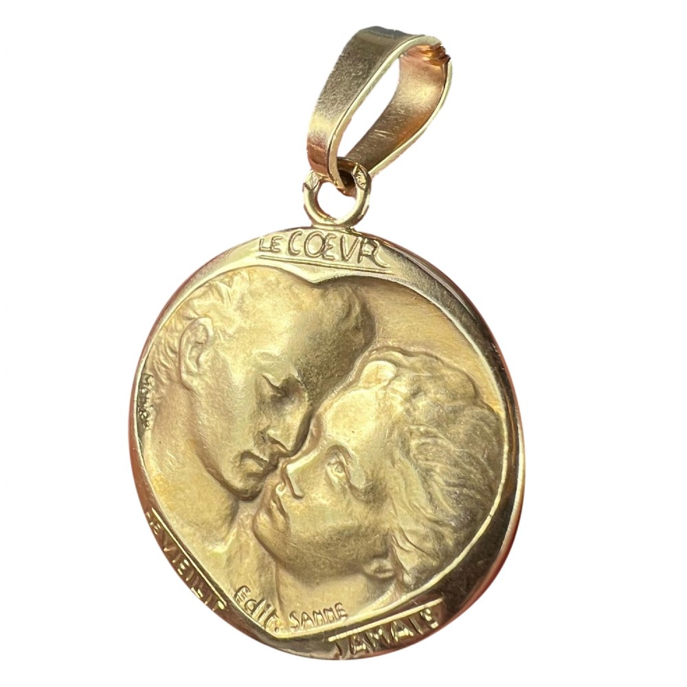 A circular 18-carat yellow gold medal pendant depicting a relief motif of two lovers kissing beneath French romantic lettering.
