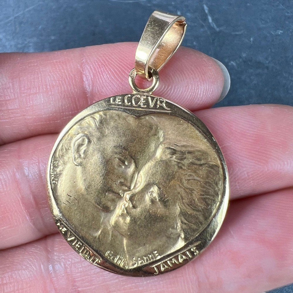 A circular 18-carat yellow gold medal pendant depicting a relief motif of two lovers kissing beneath French romantic lettering. View V