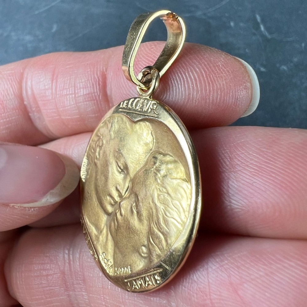 A circular 18-carat yellow gold medal pendant depicting a relief motif of two lovers kissing beneath French romantic lettering. View VII