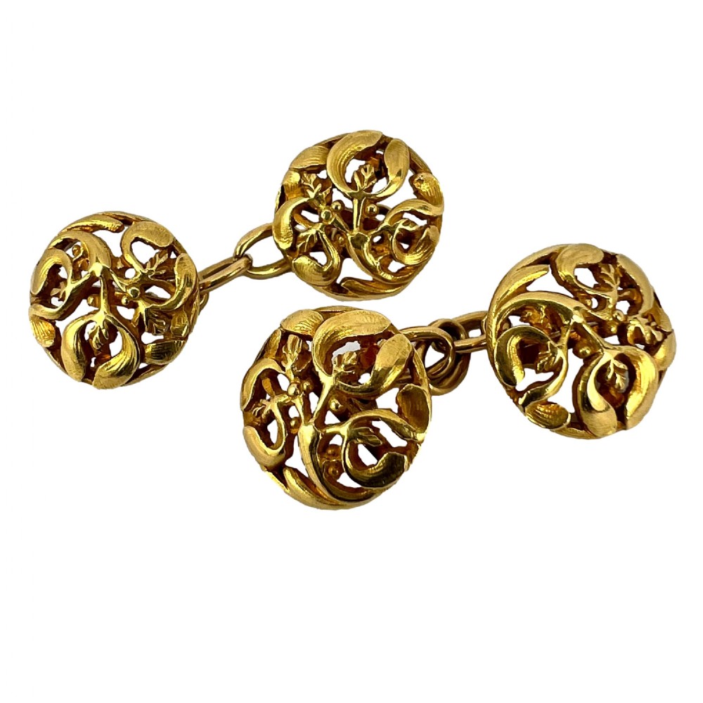 A pair of circular 18-carat yellow gold Art Nouveau cufflinks featuring pierced openwork mistletoe leaf motifs connected by chain links.
