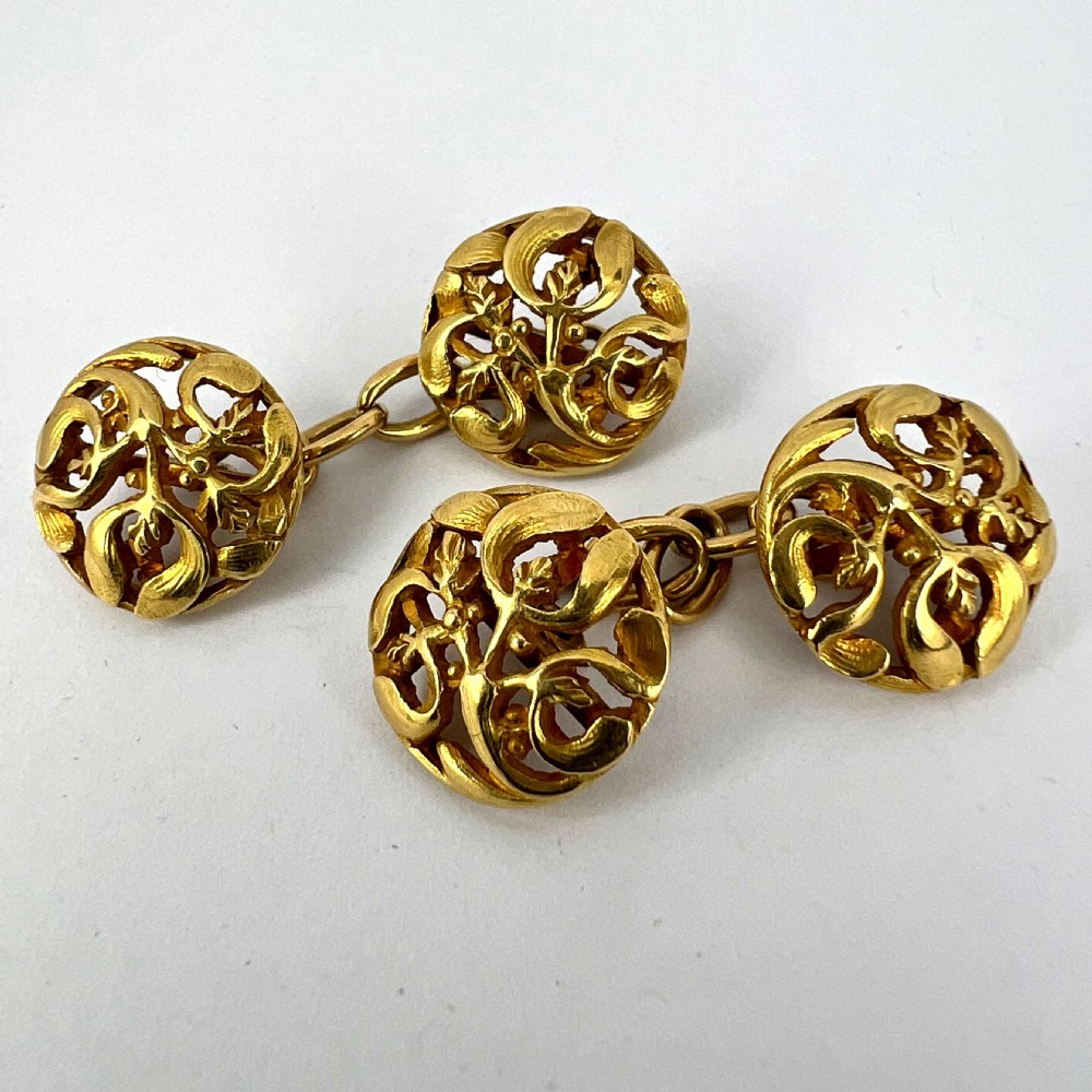 A pair of circular 18-carat yellow gold Art Nouveau cufflinks featuring pierced openwork mistletoe leaf motifs connected by chain links. View XVII