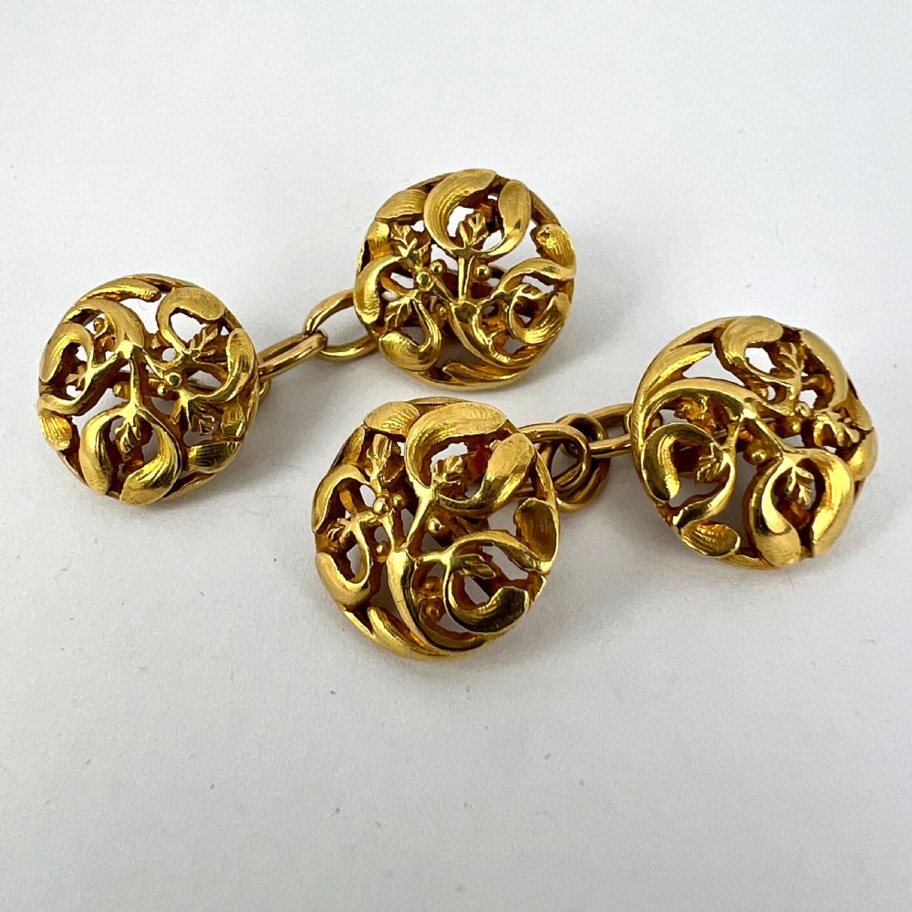 A pair of circular 18-carat yellow gold Art Nouveau cufflinks featuring pierced openwork mistletoe leaf motifs connected by chain links. View XVIII