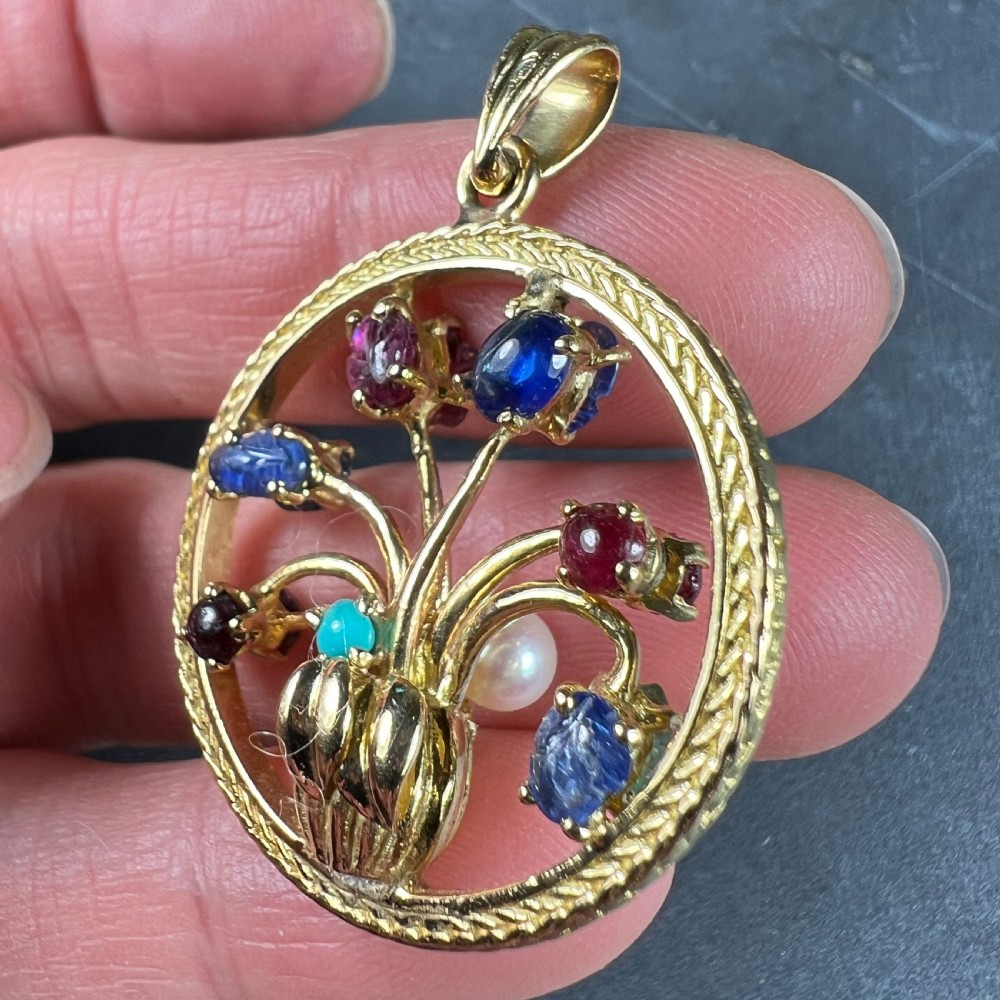 A circular 18-carat yellow gold pendant featuring an openwork flower vase design set with carved rubies, sapphires, an emerald, and a central pearl. View XI