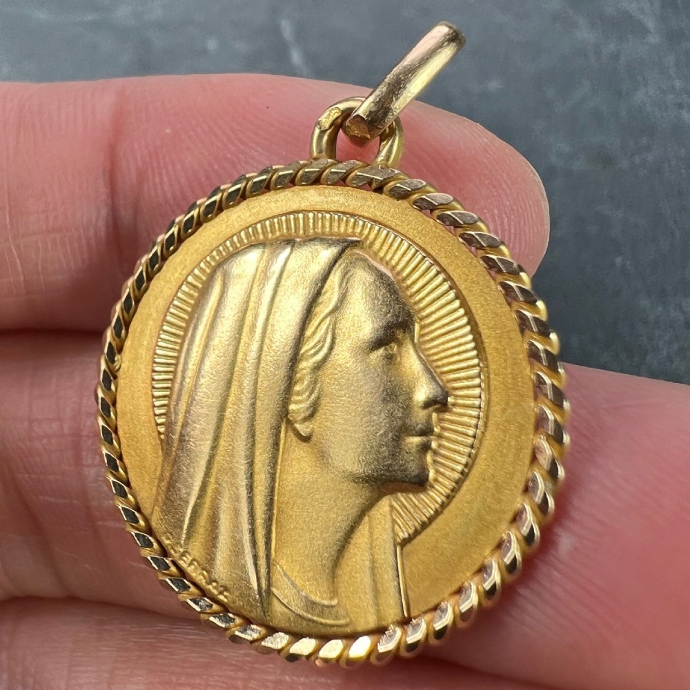 A circular 18ct yellow gold medal pendant featuring a profile relief of the Virgin Mary with a rayed halo and a rope-twist border. View VI