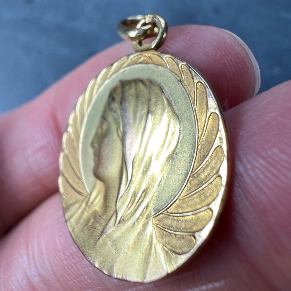 A circular 18K yellow gold medal pendant depicting a side profile of the Virgin Mary surrounded by stylised wing motifs. View VIII