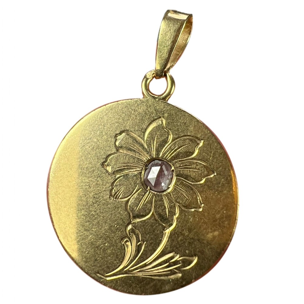 A circular 18 karat yellow gold pendant featuring an engraved daisy flower motif with a centrally set diamond and a top hanging bail.
