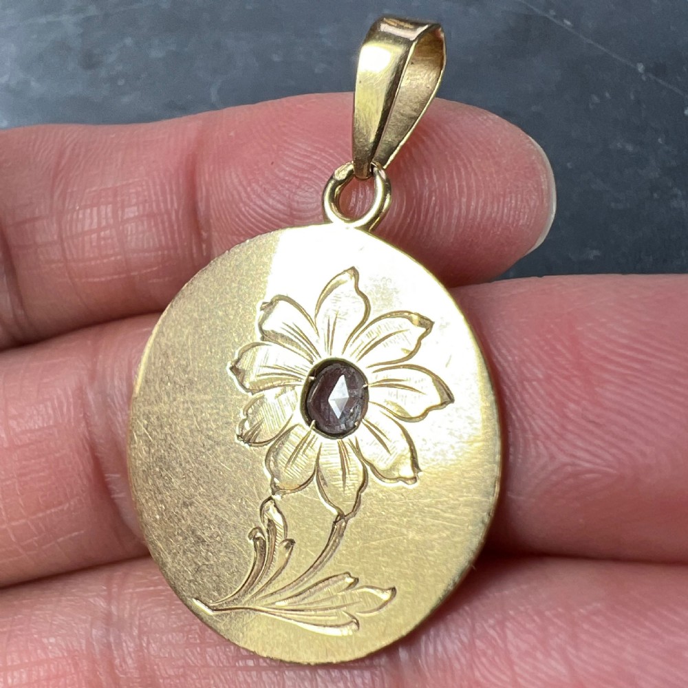 A circular 18 karat yellow gold pendant featuring an engraved daisy flower motif with a centrally set diamond and a top hanging bail. View VI