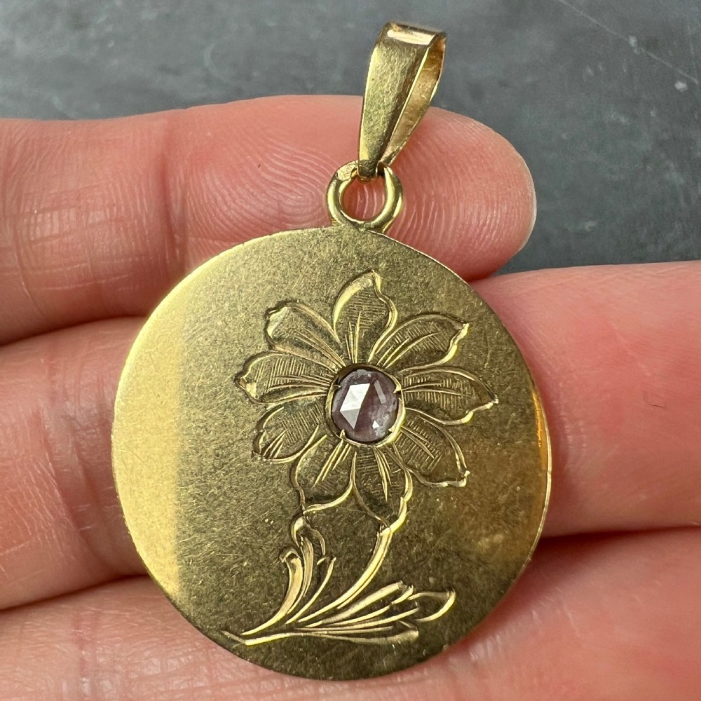 A circular 18 karat yellow gold pendant featuring an engraved daisy flower motif with a centrally set diamond and a top hanging bail. View VII