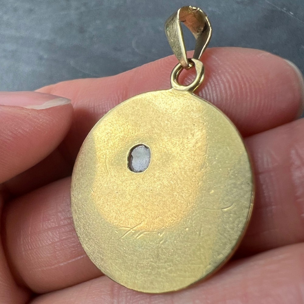 A circular 18 karat yellow gold pendant featuring an engraved daisy flower motif with a centrally set diamond and a top hanging bail. View X