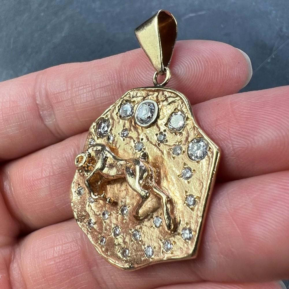 A textured 14k yellow gold astrological pendant featuring an embossed horned animal motif set with small diamonds representing stars. View VII