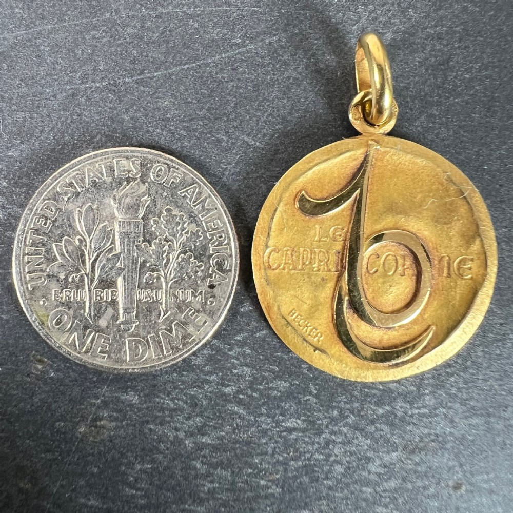 A circular 18K yellow gold zodiac charm pendant featuring the embossed Capricorn symbol and French text Le Capricorne signed Becker. View X