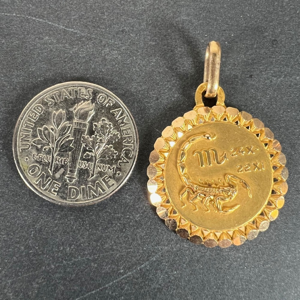 A circular 18ct yellow gold Scorpio zodiac pendant featuring an embossed scorpion, astrological symbol, and a faceted sunburst border. View X