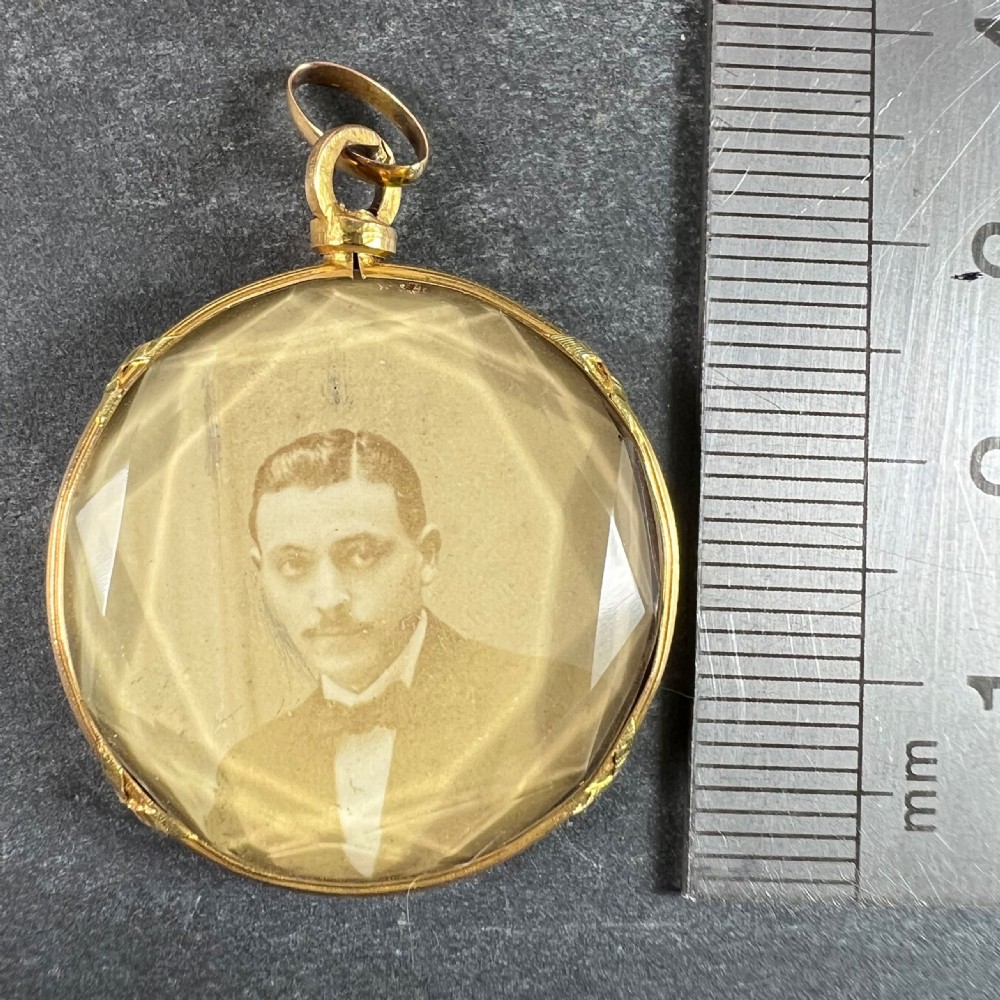 A circular 18ct yellow gold pendant featuring a faceted glass front enclosing a monochrome portrait photograph of a man. View XII