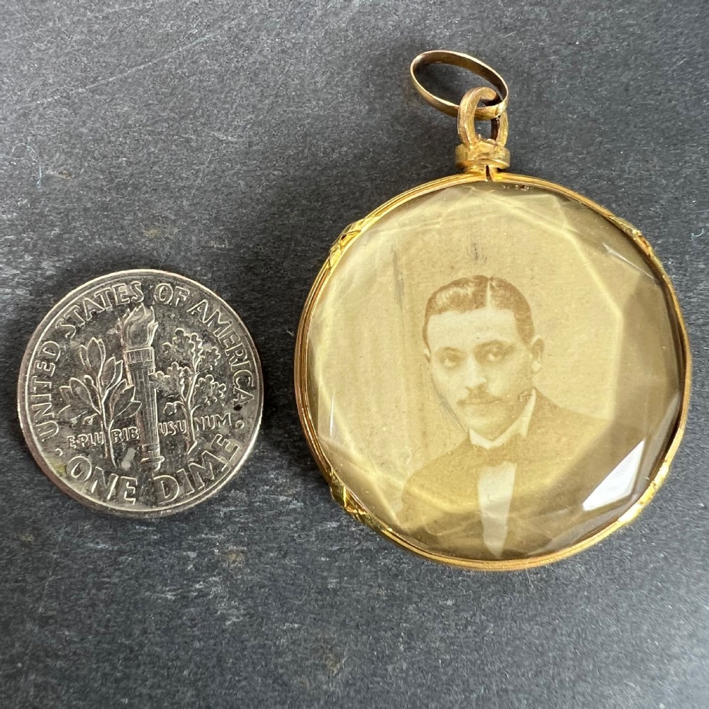 A circular 18ct yellow gold pendant featuring a faceted glass front enclosing a monochrome portrait photograph of a man. View XIII