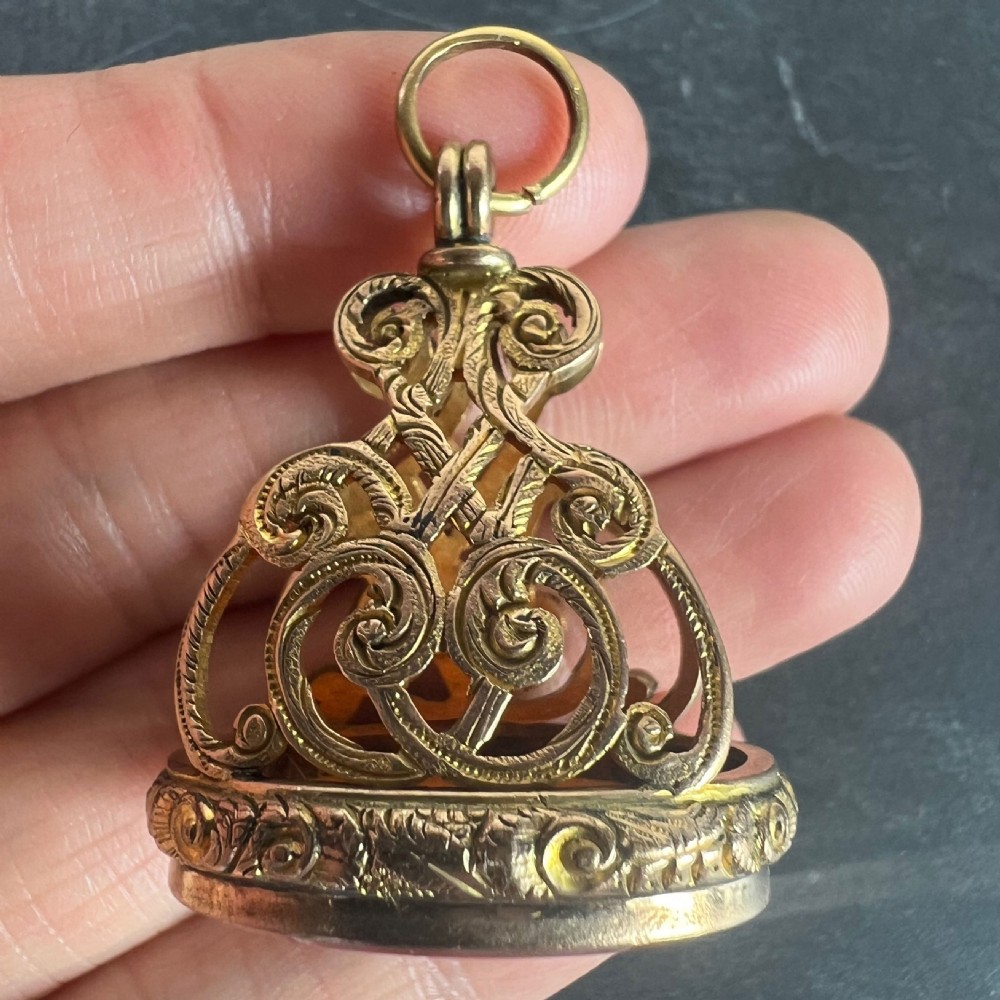 An ornate Victorian yellow gold fob seal featuring elaborate scrollwork openwork and a smooth oval carnelian base suspended from a gold ring. View VII