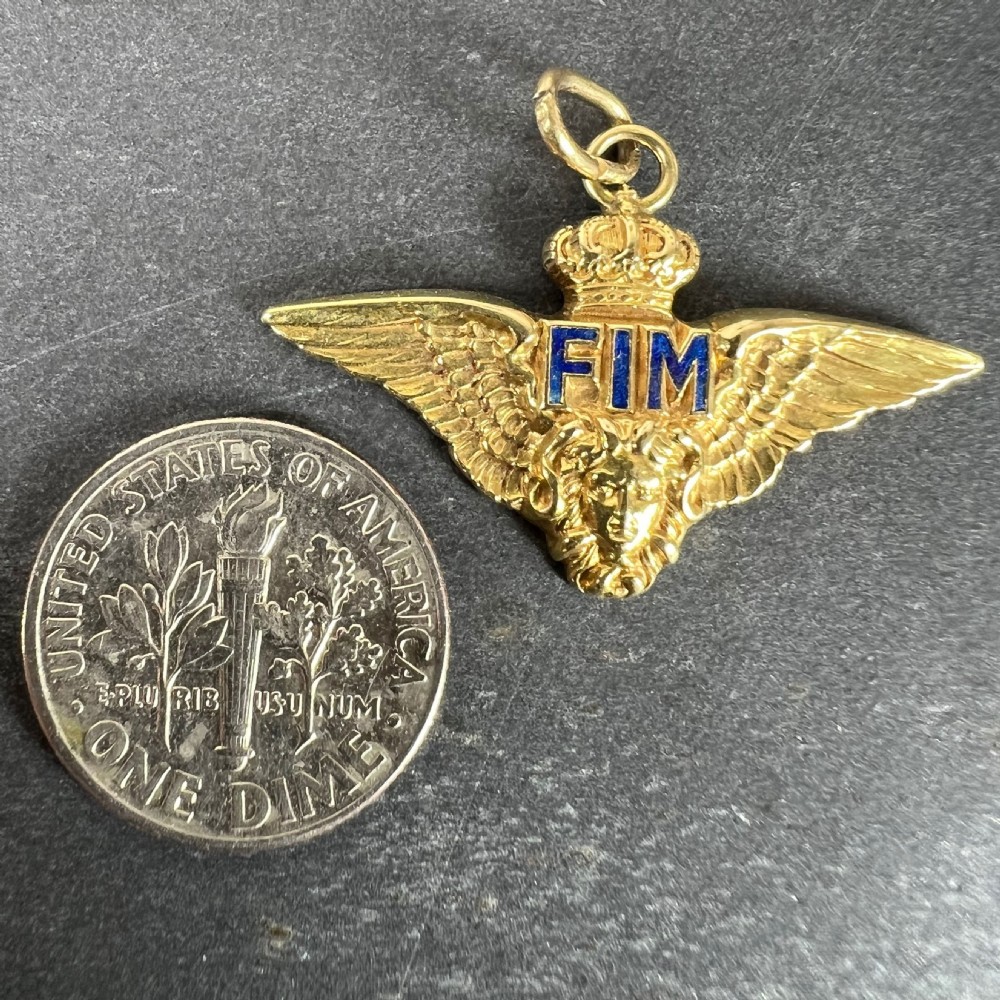 An 18k yellow gold pendant featuring outspread wings topped with a crown, a lion head motif at the base, and blue enamel letters. View XI
