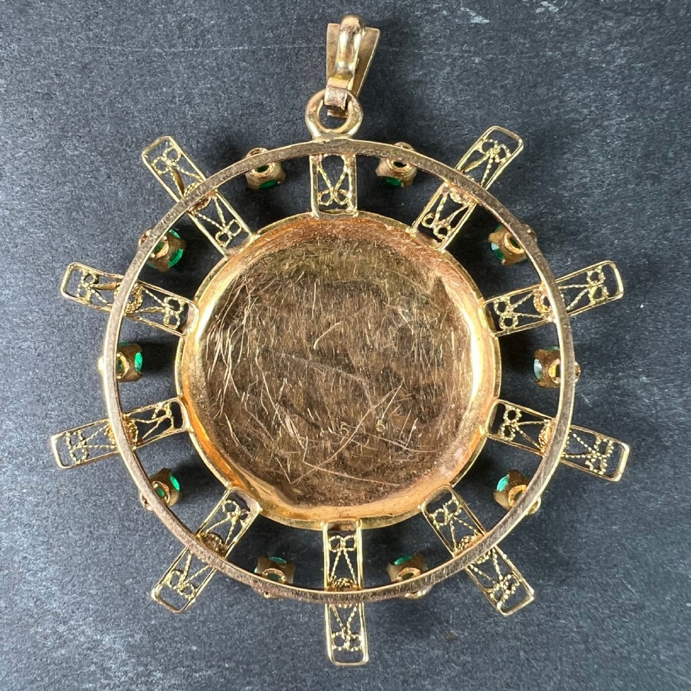 A circular 18ct yellow gold locket featuring central floral engraving and a radiating sunburst frame set with round green emeralds. View III