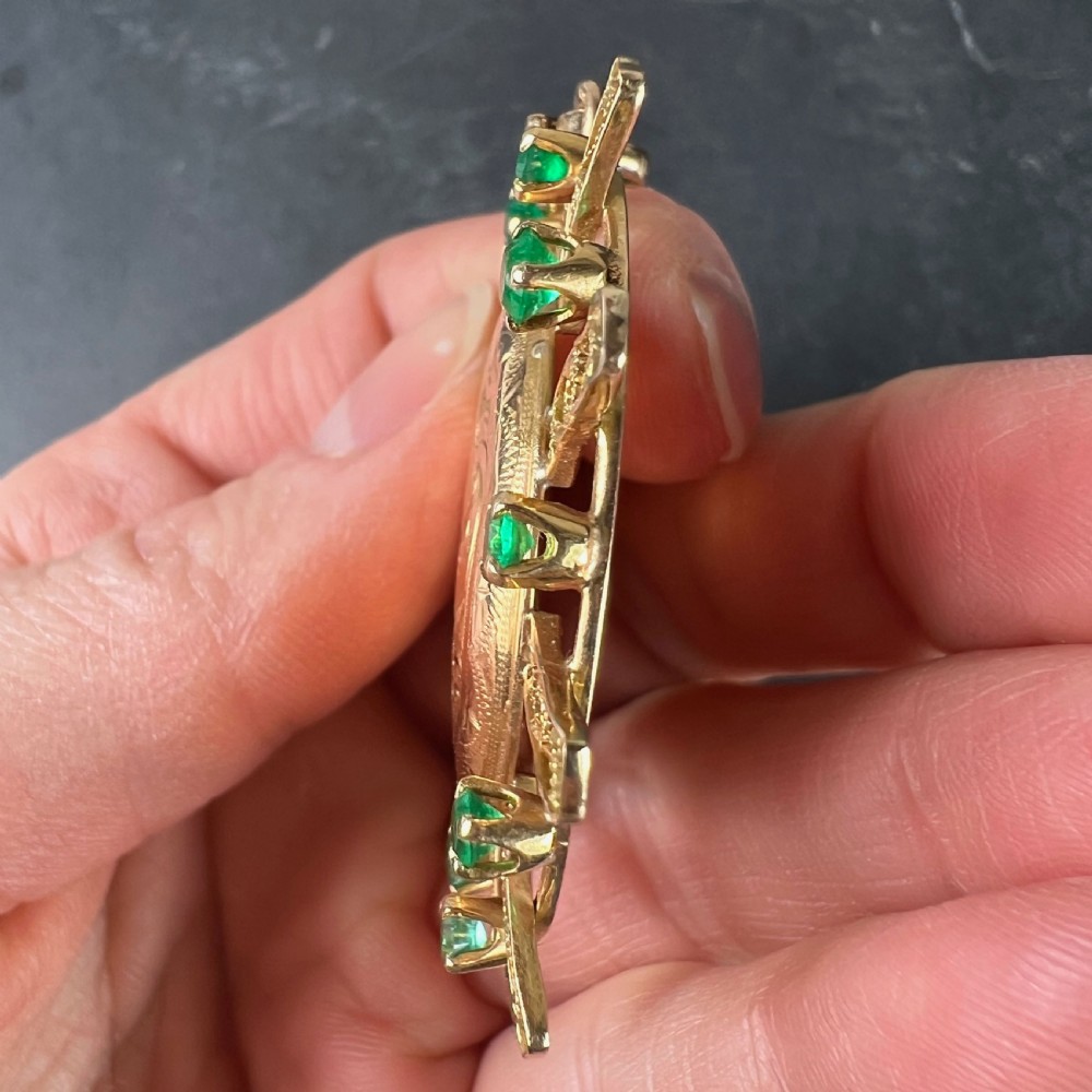 A circular 18ct yellow gold locket featuring central floral engraving and a radiating sunburst frame set with round green emeralds. View VIII