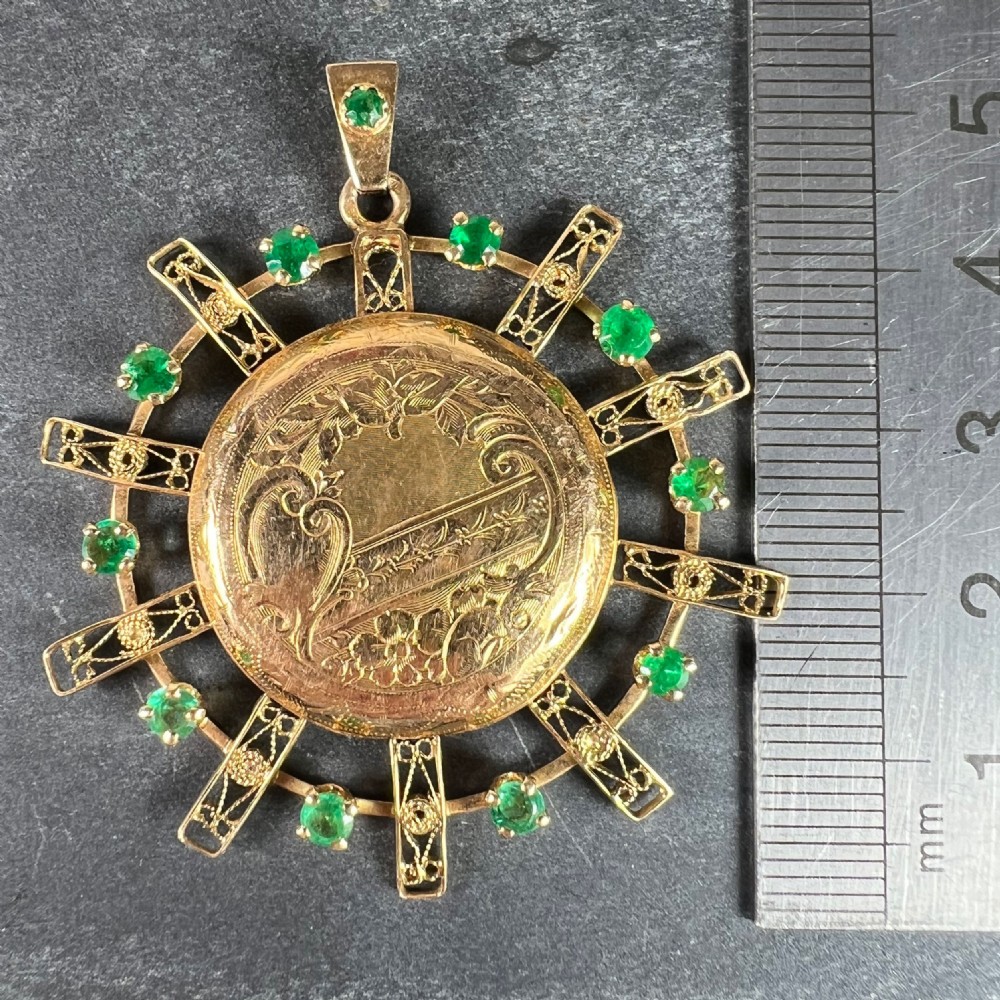 A circular 18ct yellow gold locket featuring central floral engraving and a radiating sunburst frame set with round green emeralds. View XI