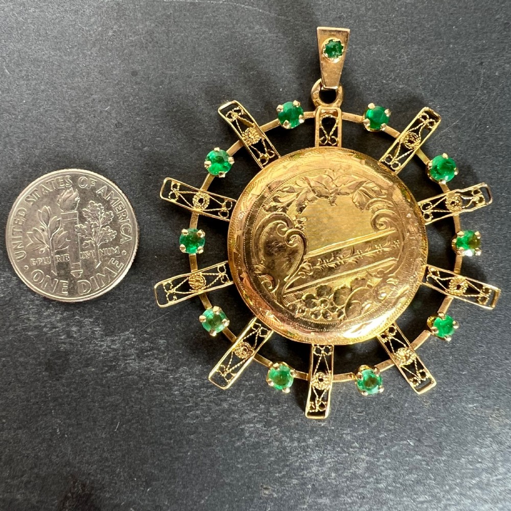 A circular 18ct yellow gold locket featuring central floral engraving and a radiating sunburst frame set with round green emeralds. View XII