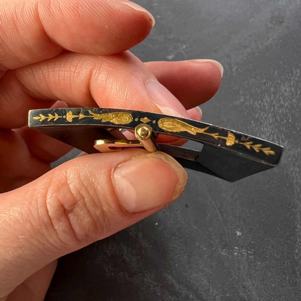 A rectangular damascene steel belt buckle decorated with gold inlaid scrollwork, cherub faces, and a double-prong central mechanism. View X