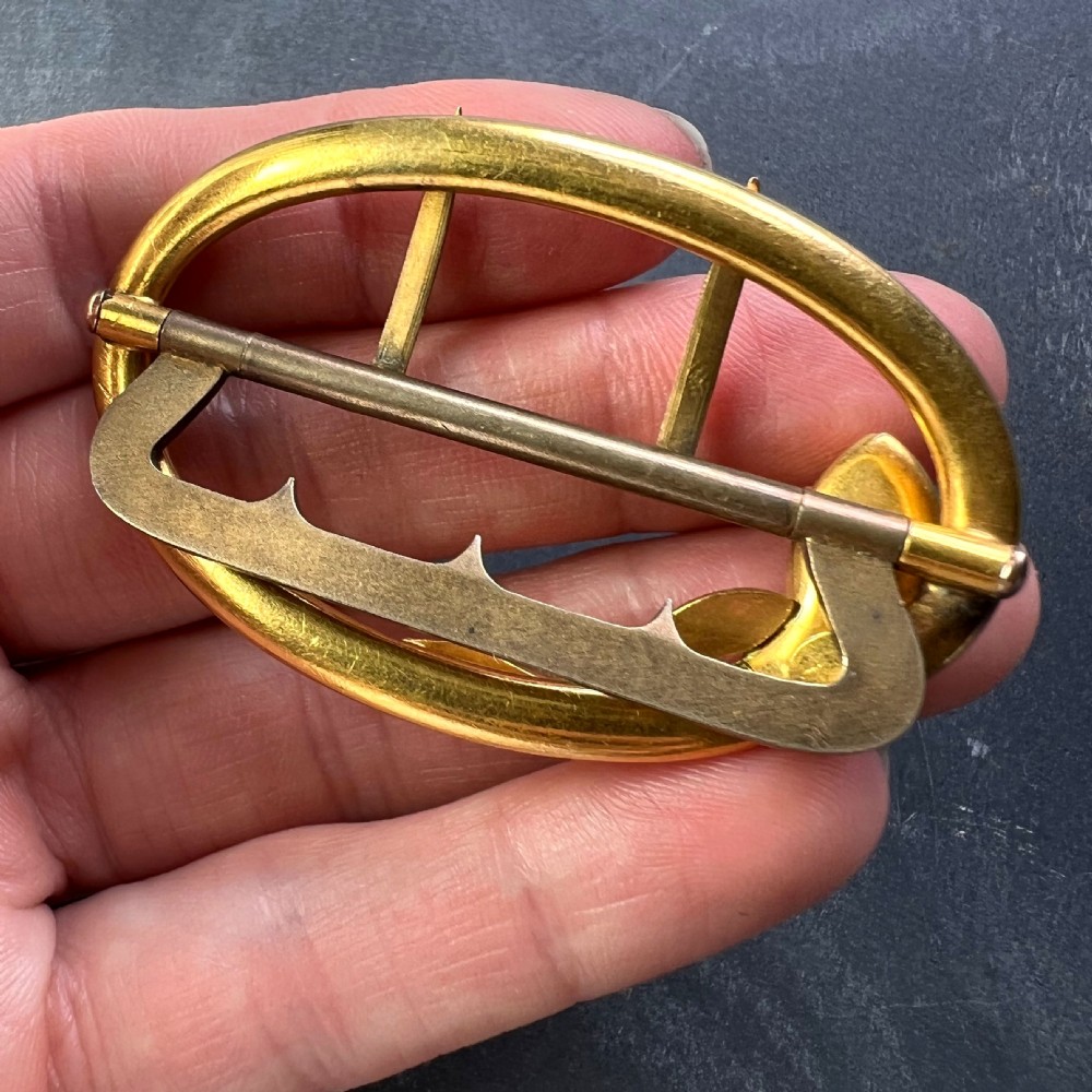 An oval 18K yellow gold belt buckle featuring a carved snake motif along the upper rim with garnet eyes. View X