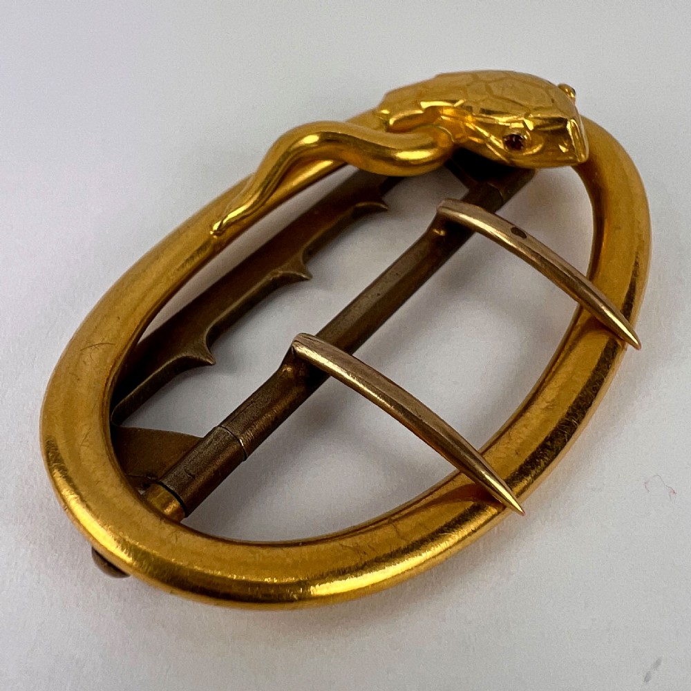 An oval 18K yellow gold belt buckle featuring a carved snake motif along the upper rim with garnet eyes. View XVII
