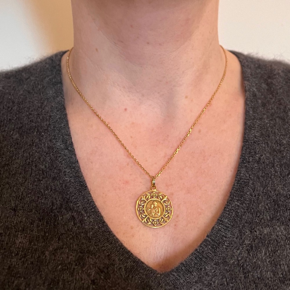 A circular 18-carat yellow gold religious pendant depicting the Madonna and Child in relief surrounded by an intricate openwork floral border. View IV