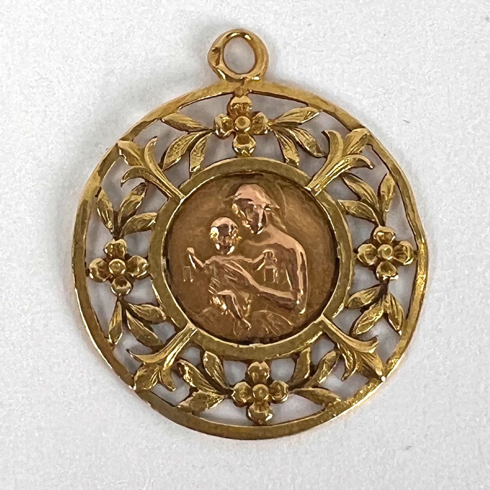 A circular 18-carat yellow gold religious pendant depicting the Madonna and Child in relief surrounded by an intricate openwork floral border. View X