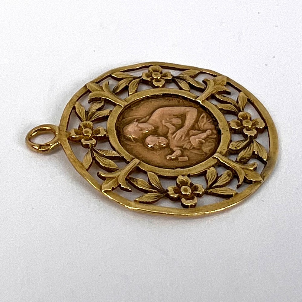 A circular 18-carat yellow gold religious pendant depicting the Madonna and Child in relief surrounded by an intricate openwork floral border. View XII