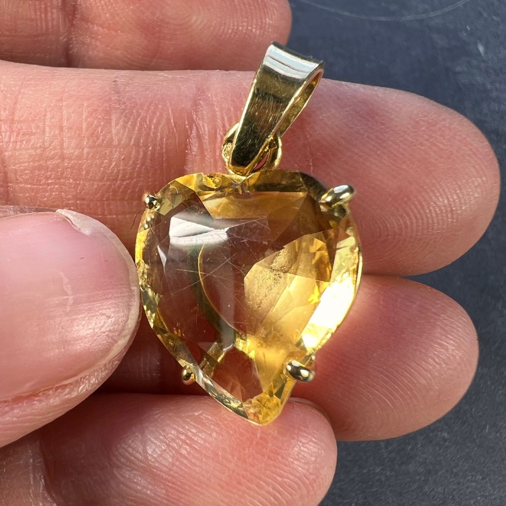 A heart-shaped faceted yellow citrine gemstone set in an eighteen-carat yellow gold claw mount with a top loop. View VI