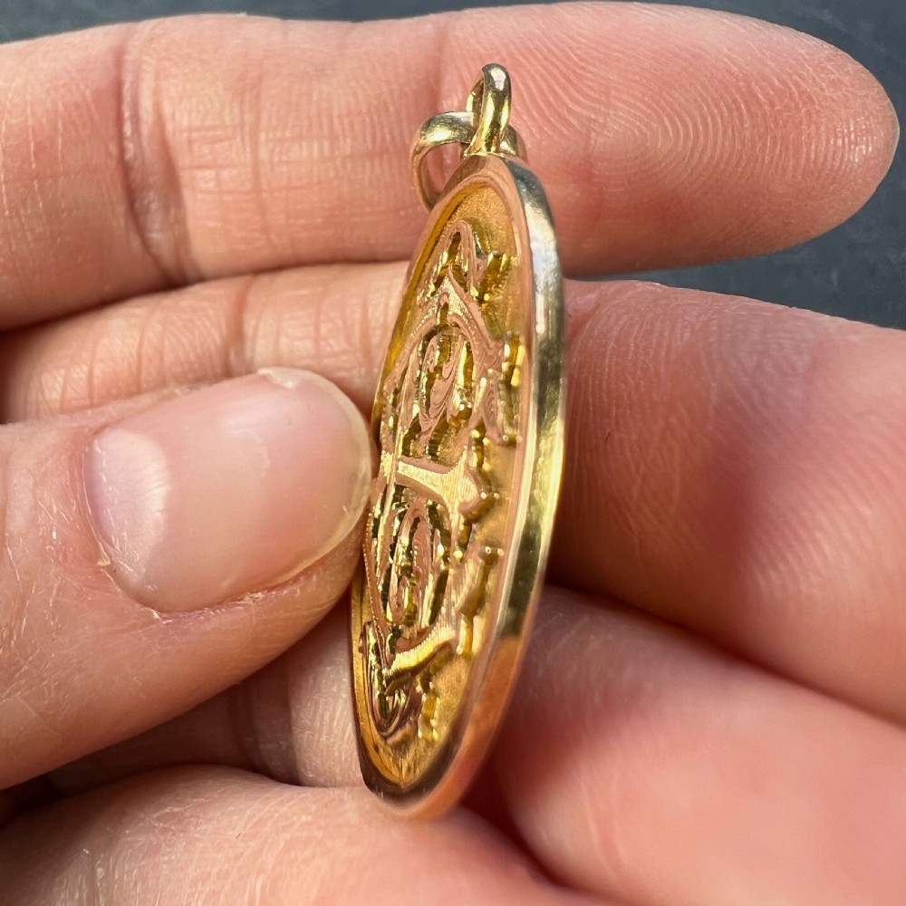 A circular 18k rose gold medal pendant featuring relief-engraved ornate monogram letters EC on a textured stippled background with a top hanging bail. View VIII