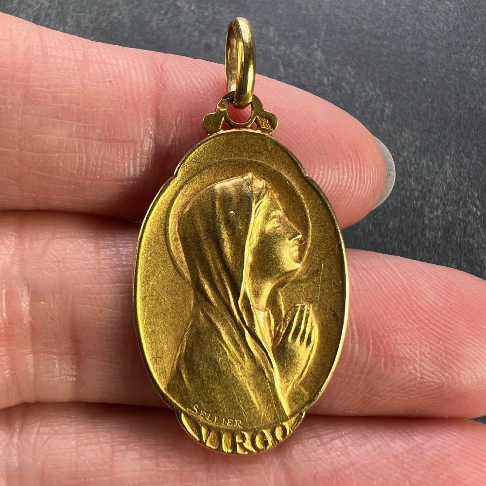 An oval 18k yellow gold religious medal depicting a profile bas-relief of the Virgin Mary in prayer with the inscription Virgo and signature Sellier. View V