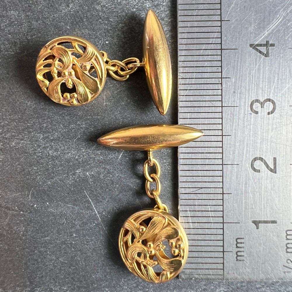 A pair of circular 18ct yellow gold Art Nouveau cufflinks featuring pierced mistletoe foliage linked by chain to torpedo-shaped backs. View X