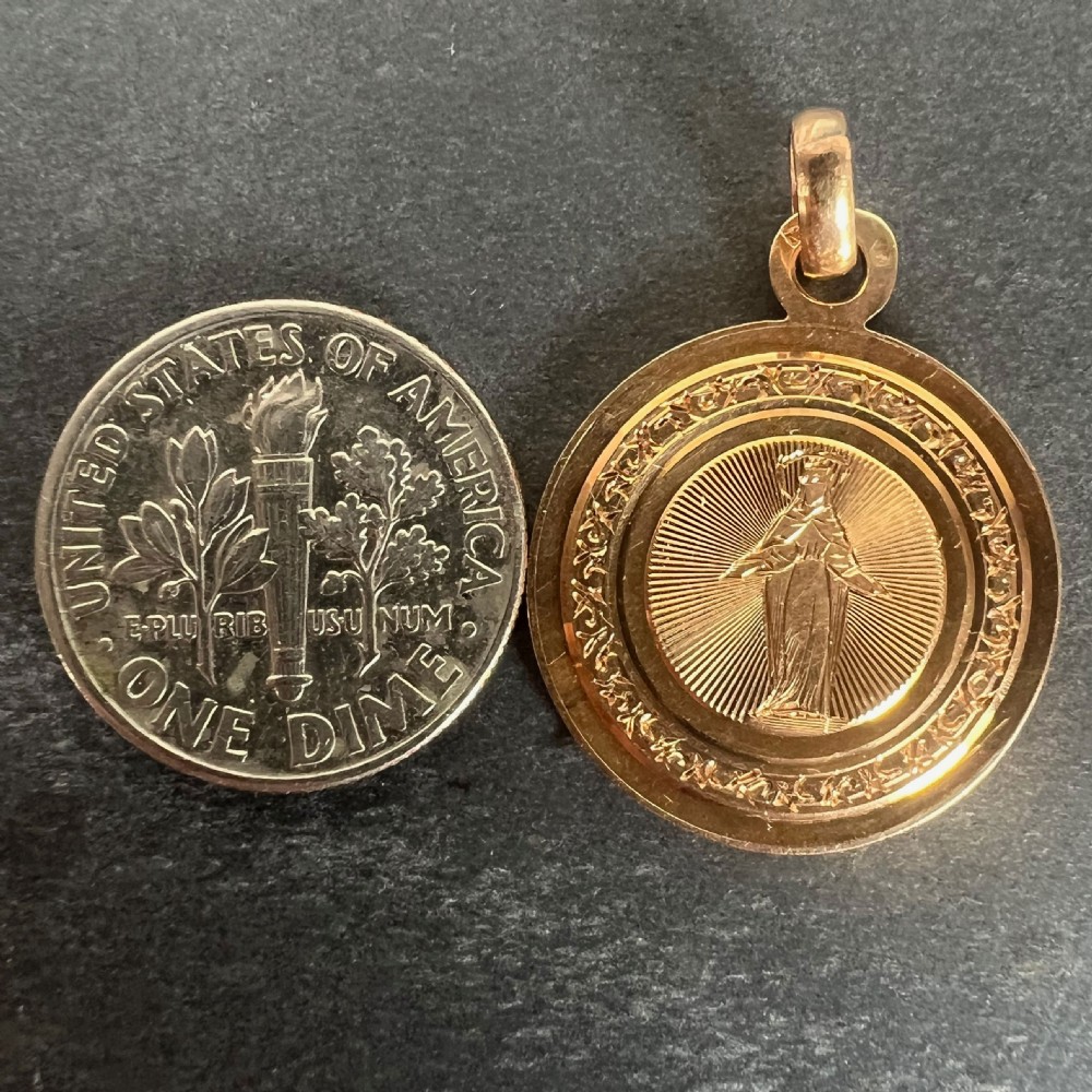 A circular 18k rose gold religious pendant depicting the Virgin Mary surrounded by radial engraved lines and a decorative border. View X