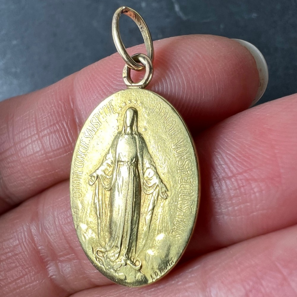 An oval 18k yellow gold pendant depicting the Virgin Mary with French devotional text embossed along the border. View VI