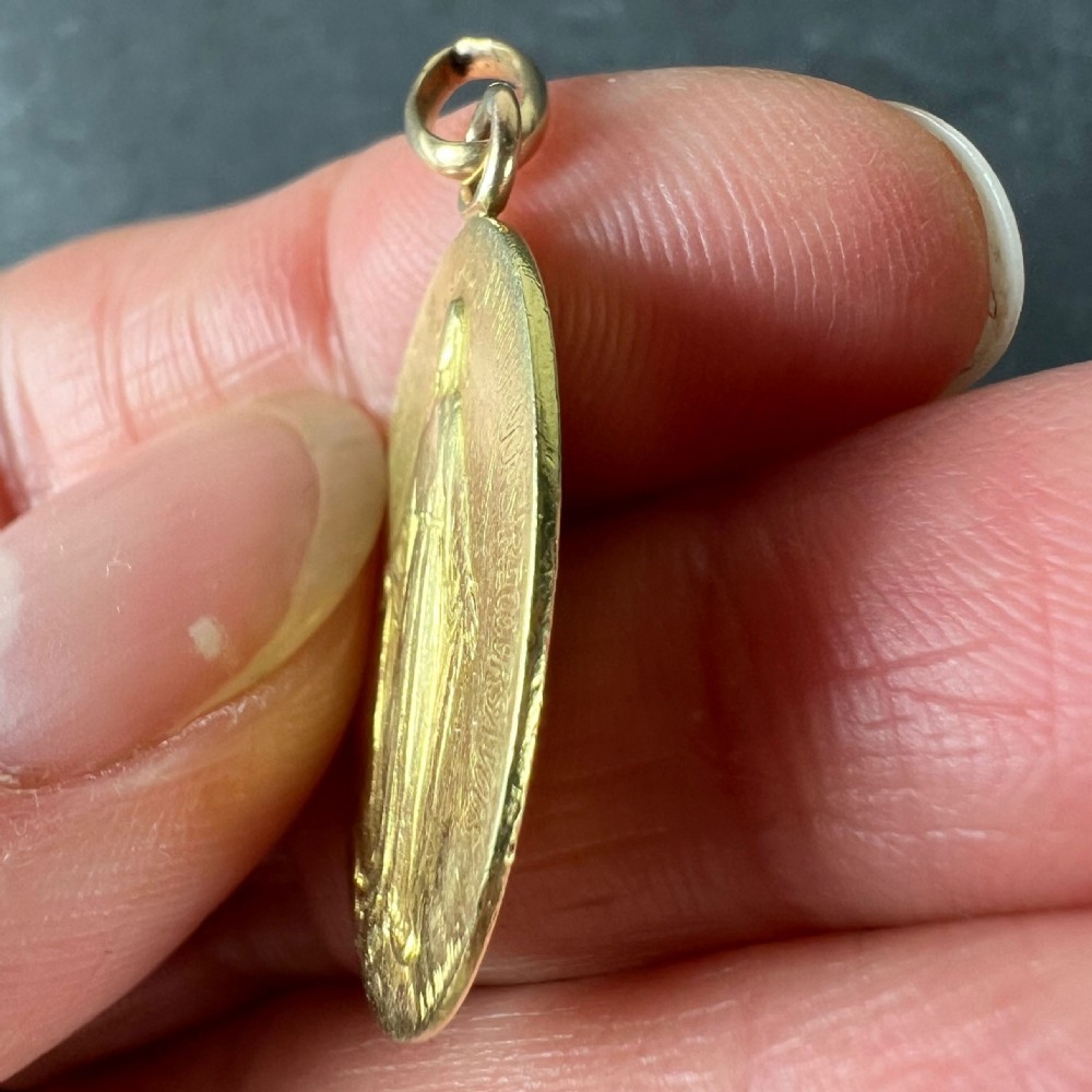 An oval 18k yellow gold pendant depicting the Virgin Mary with French devotional text embossed along the border. View VII