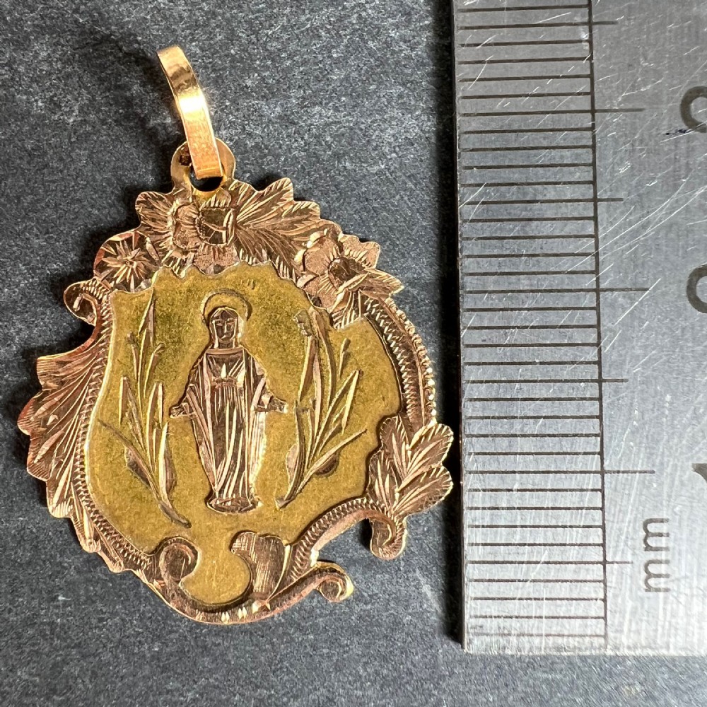 An antique French 18K yellow and rose gold religious pendant featuring an engraved Virgin Mary surrounded by a textured floral border. View X